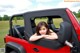 A woman sitting in the back seat of a red jeep.