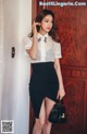 A woman standing in front of a wooden door holding a handbag.