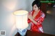 A woman in a red kimono standing next to a lamp.