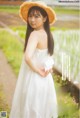 A woman in a white dress and straw hat holding a white card.